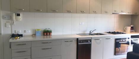 A modern kitchen with white cabinets, a dishwasher, an oven, and a sink.