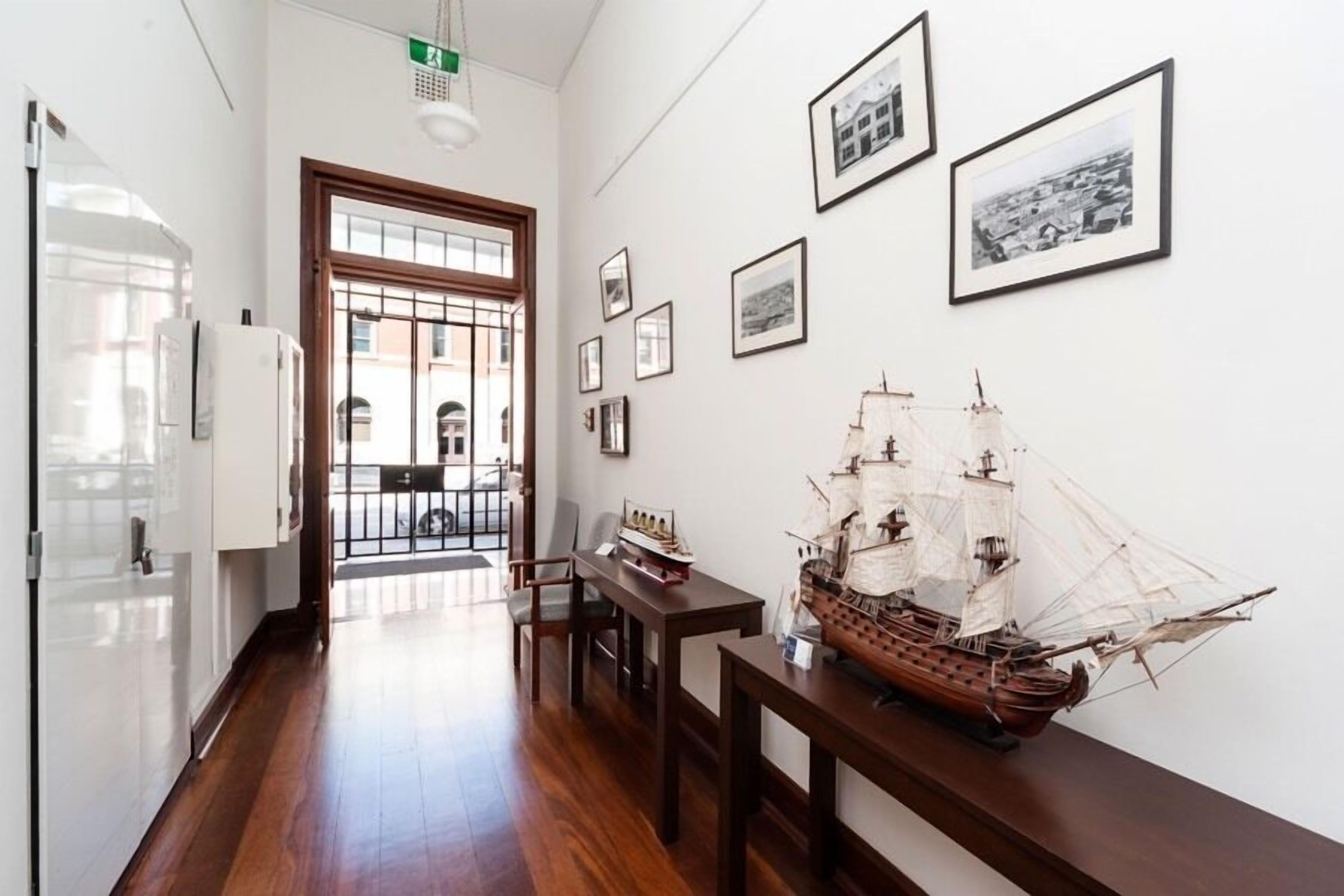A hallway with wooden flooring, a model ship on a table, and framed pictures on the wall.