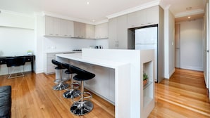 A modern kitchen with white cabinets, a central island with bar stools, and a built-in refrigerator. - Fremantle Harbourside  Apartments (Fremantle)