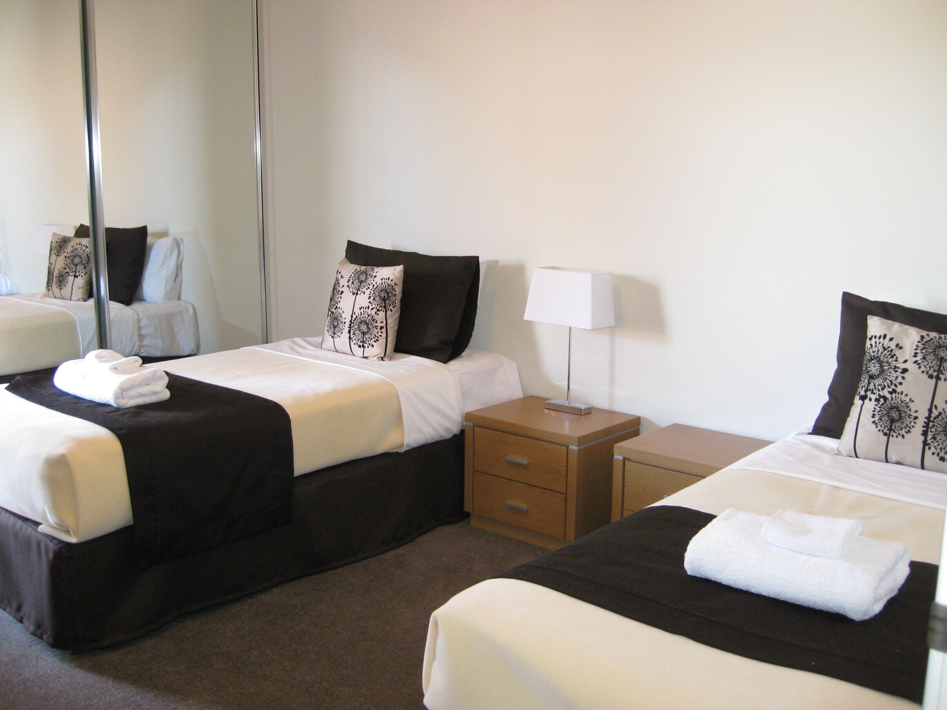 Habitación de hotel con dos camas individuales, cada una con una almohada y una mesita de noche.