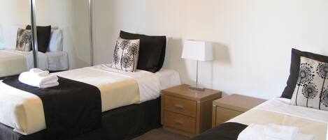 Habitación de hotel con dos camas individuales, cada una con una almohada y una mesita de noche.