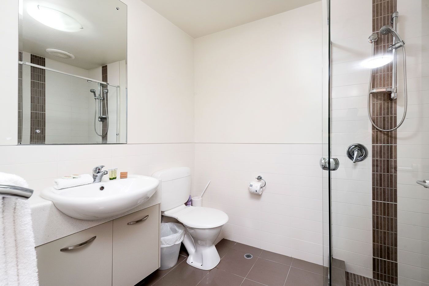 Een moderne badkamer met een witte wastafel, toilet en douchecabine met glazen wanden.