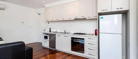 A modern kitchen with white cabinets, stainless steel appliances, and a black sofa.