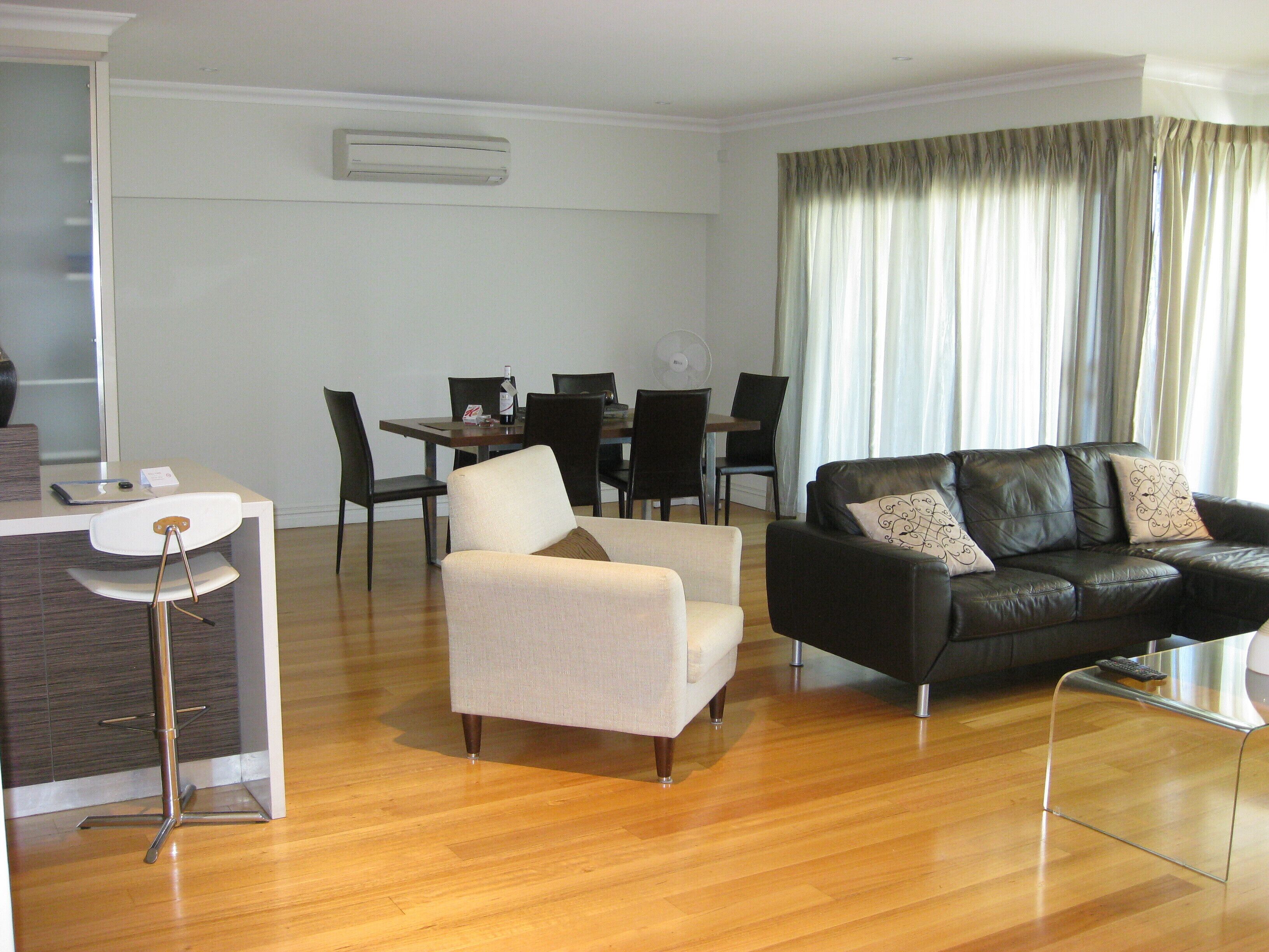 A modern living room with a dining area, featuring a sofa, armchairs, a dining table, and chairs.