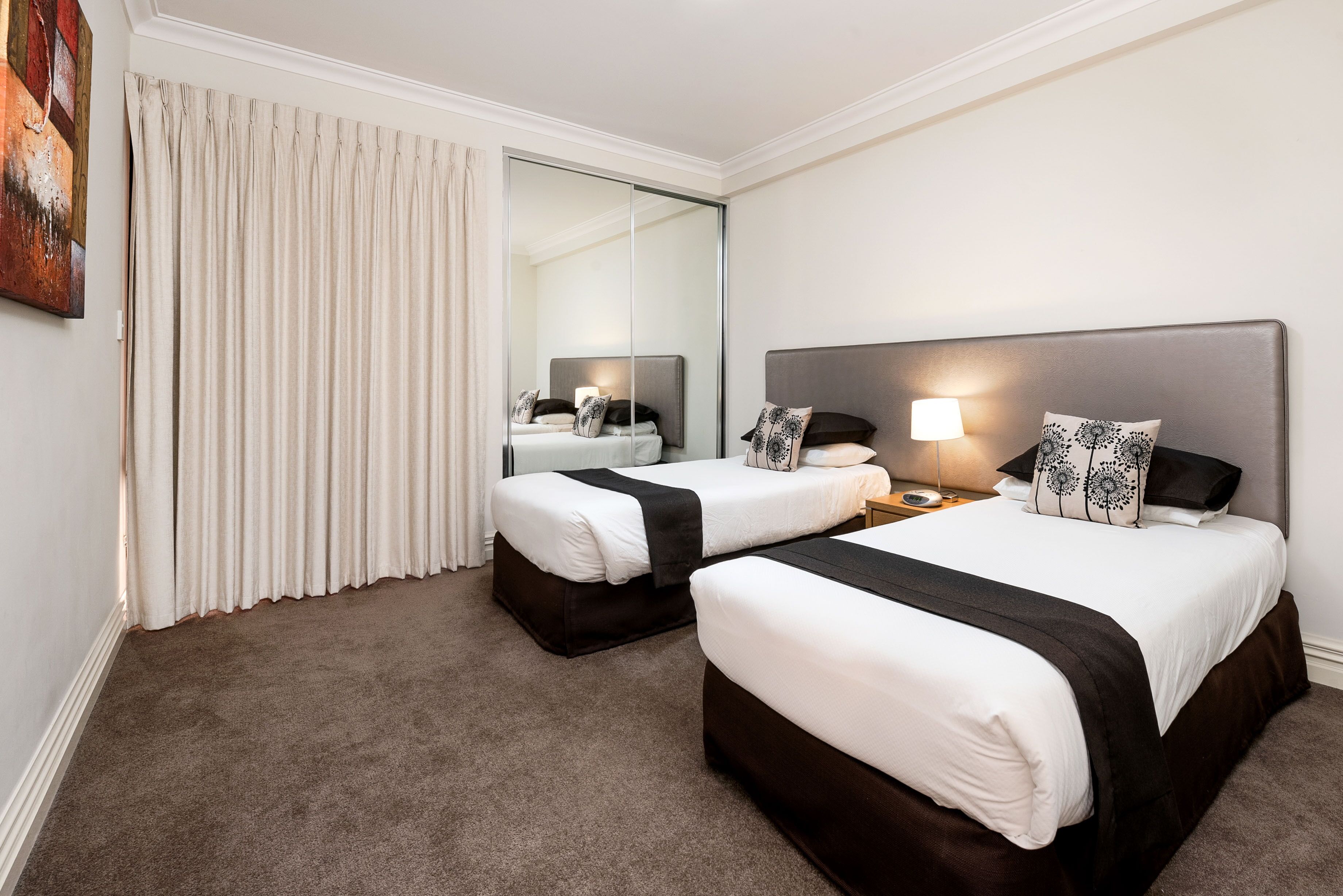 A hotel room with two beds, a large mirror, a nightstand with a lamp, and a carpeted floor.