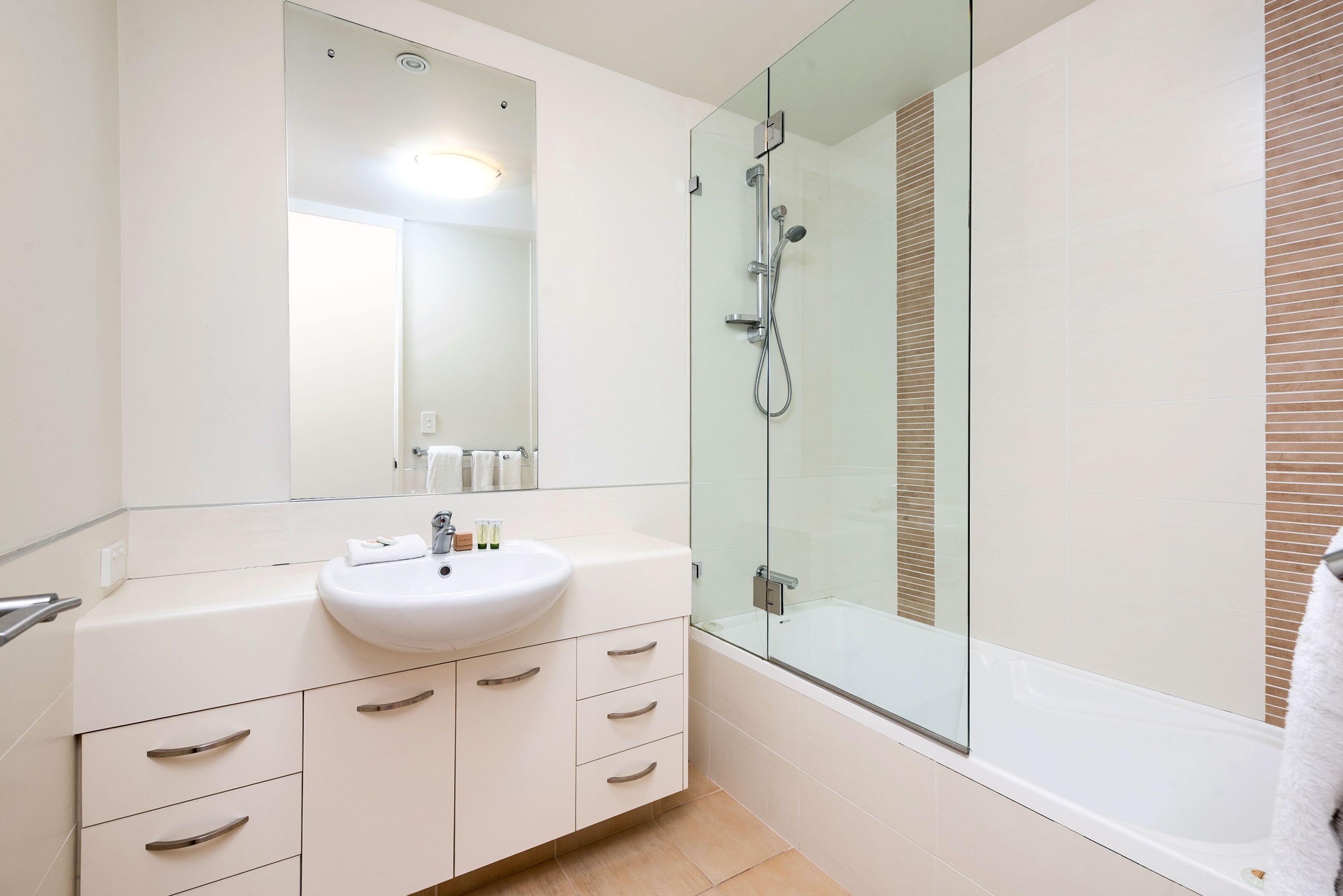 A modern bathroom with a glass-enclosed shower, a white sink, and a large mirror.