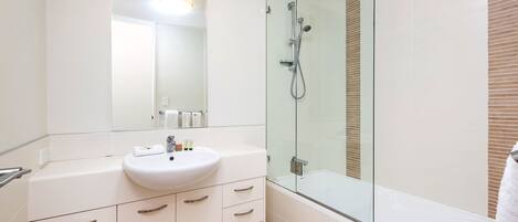 A modern bathroom with a glass-enclosed shower, a white sink, and a large mirror.