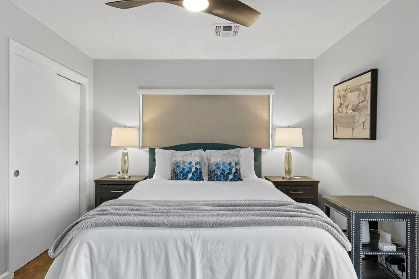 A hotel room with a bed, two bedside tables with lamps, a ceiling fan, and a framed picture on the wall.