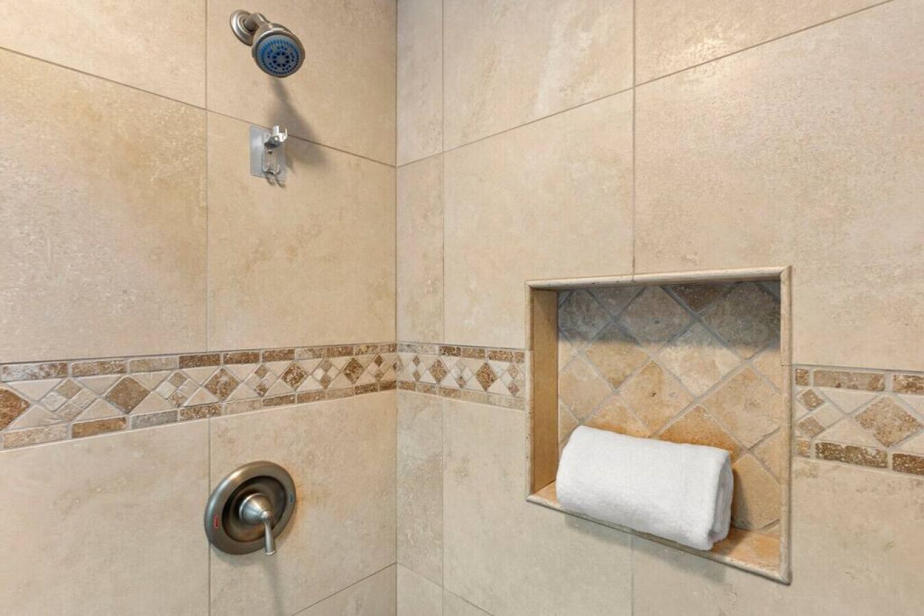 A shower area with a glass shelf holding a towel, a showerhead, and a control knob.