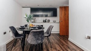 Ein moderner Essbereich mit einem runden Tisch und vier Stühlen, im Hintergrund eine Küche und Holzboden.