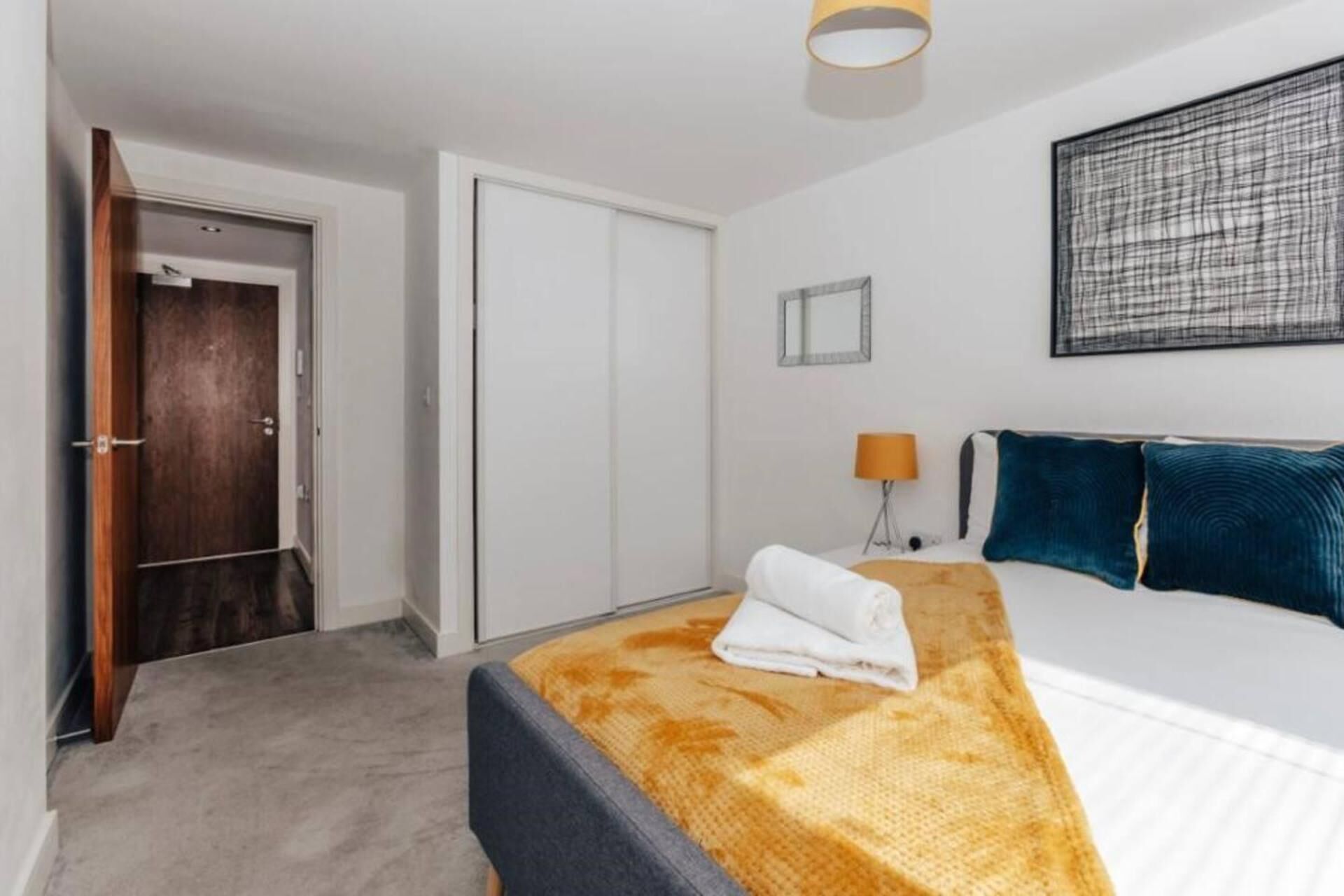 Habitación de hotel con cama, mesita de noche, lámpara, armario y una obra de arte enmarcada en la pared.