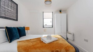 Ein modernes Schlafzimmer mit Bett, Fenster, Kleiderschrank und einem kleinen Tisch mit Pflanze.