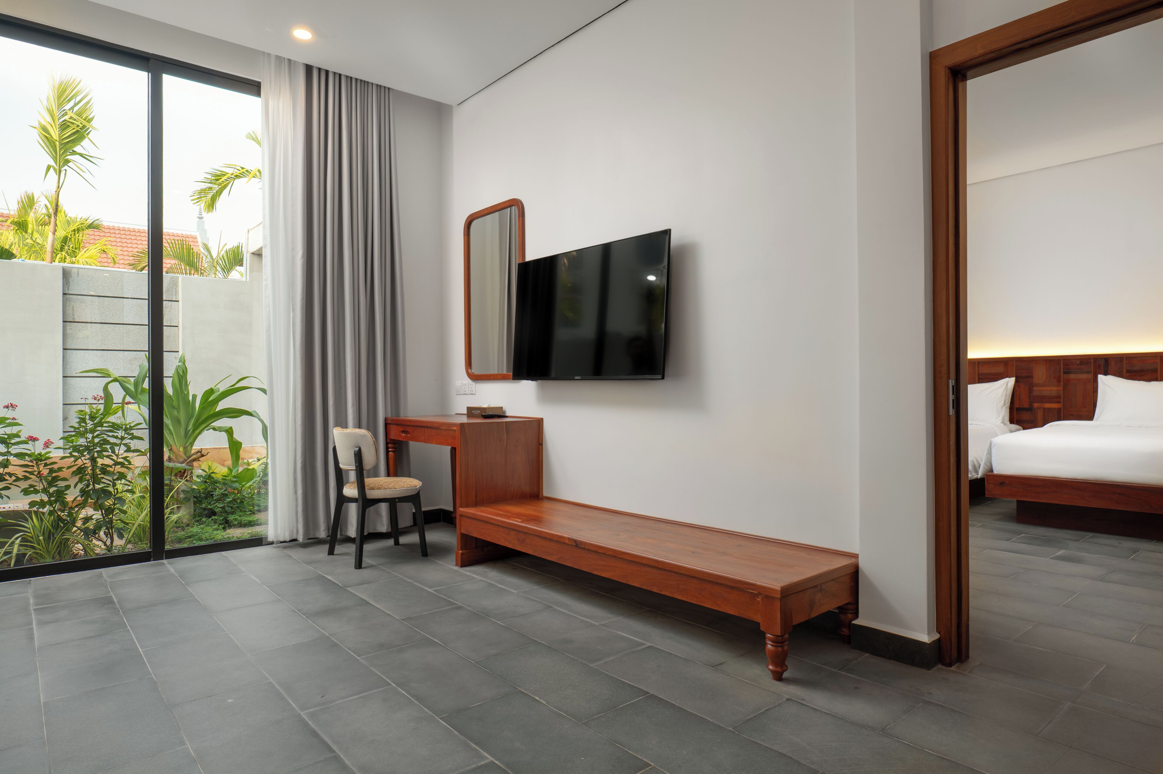 Ein modernes Hotelzimmer mit großem Fenster, Flachbildfernseher, einer Holzbank, einem Schreibtisch und einem Bett.