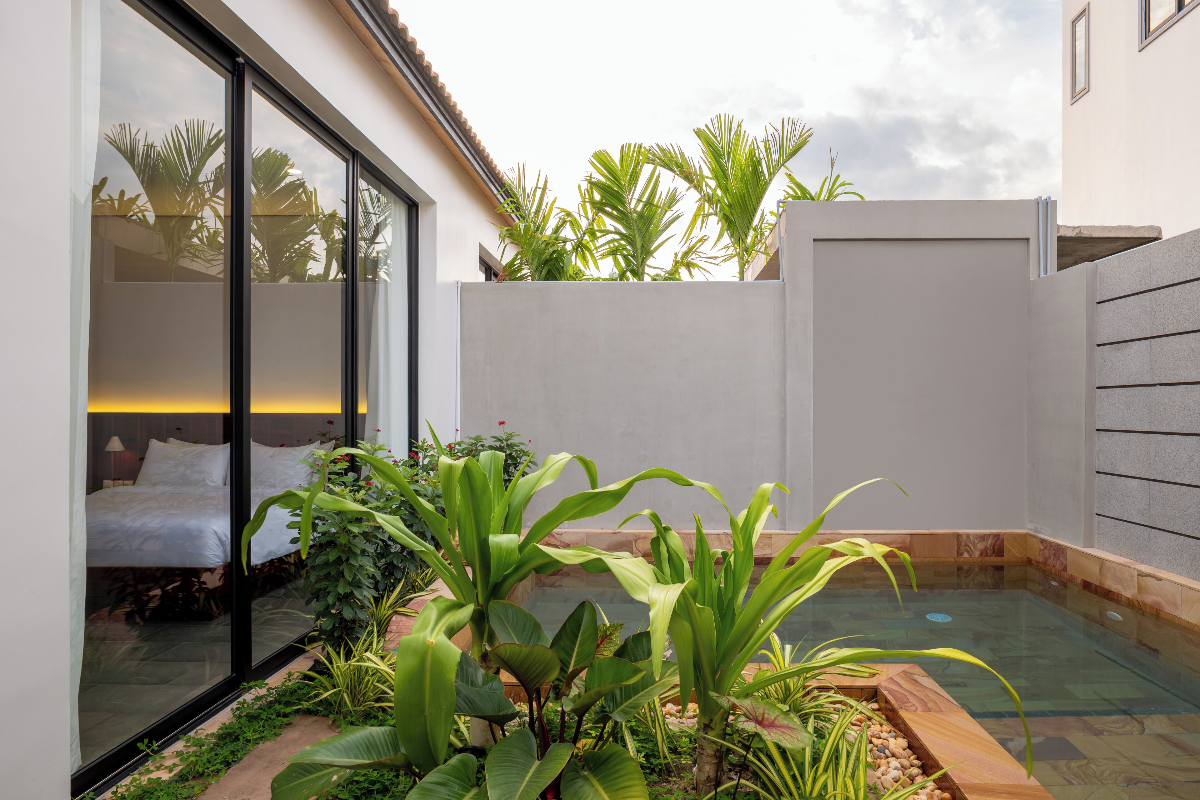 Habitación de hotel moderna con un amplio ventanal, una cama y un pequeño jardín interior con plantas y una fuente de agua.