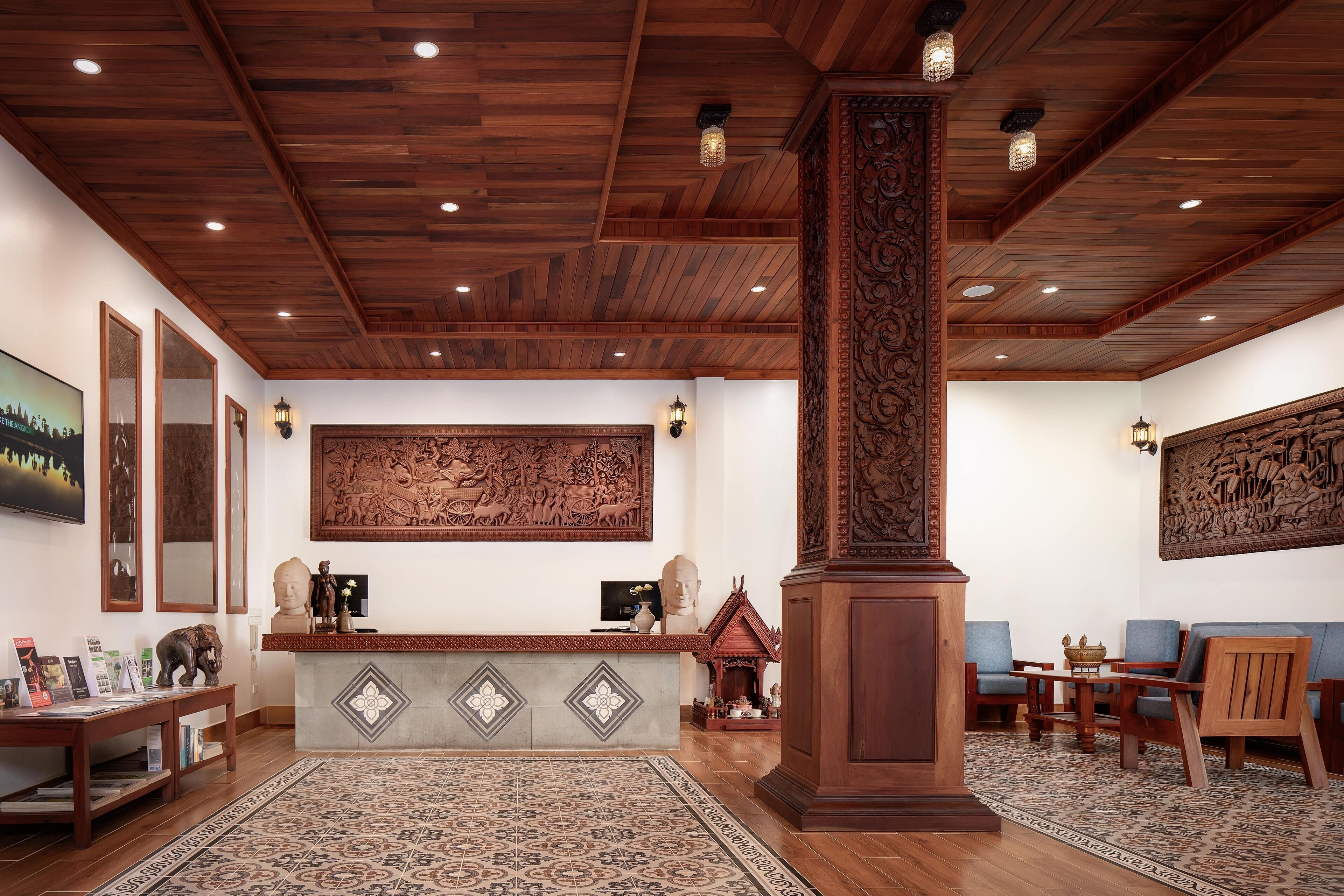 A reception area with a wooden ceiling, a reception desk, and a large wall mural. There are two blue chairs and a wooden pillar in the center.