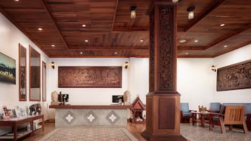 A reception area with a wooden ceiling, a reception desk, and a large wall mural. There are two blue chairs and a wooden pillar in the center.