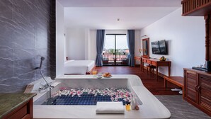 Camera d'albergo con una vasca da bagno grande, un letto, una scrivania con la TV e un balcone con vista.