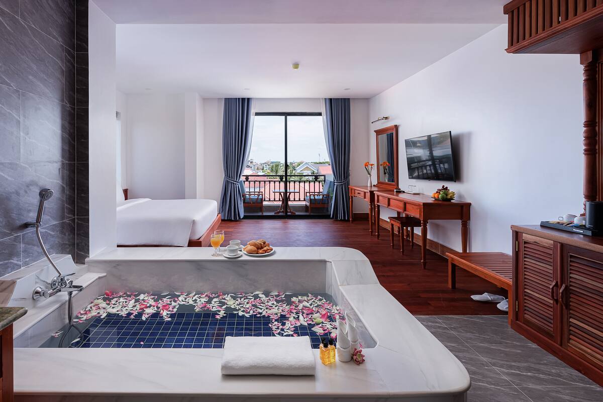 Une chambre d’hôtel avec une grande baignoire, un lit, un bureau avec une télévision et un balcon avec vue.