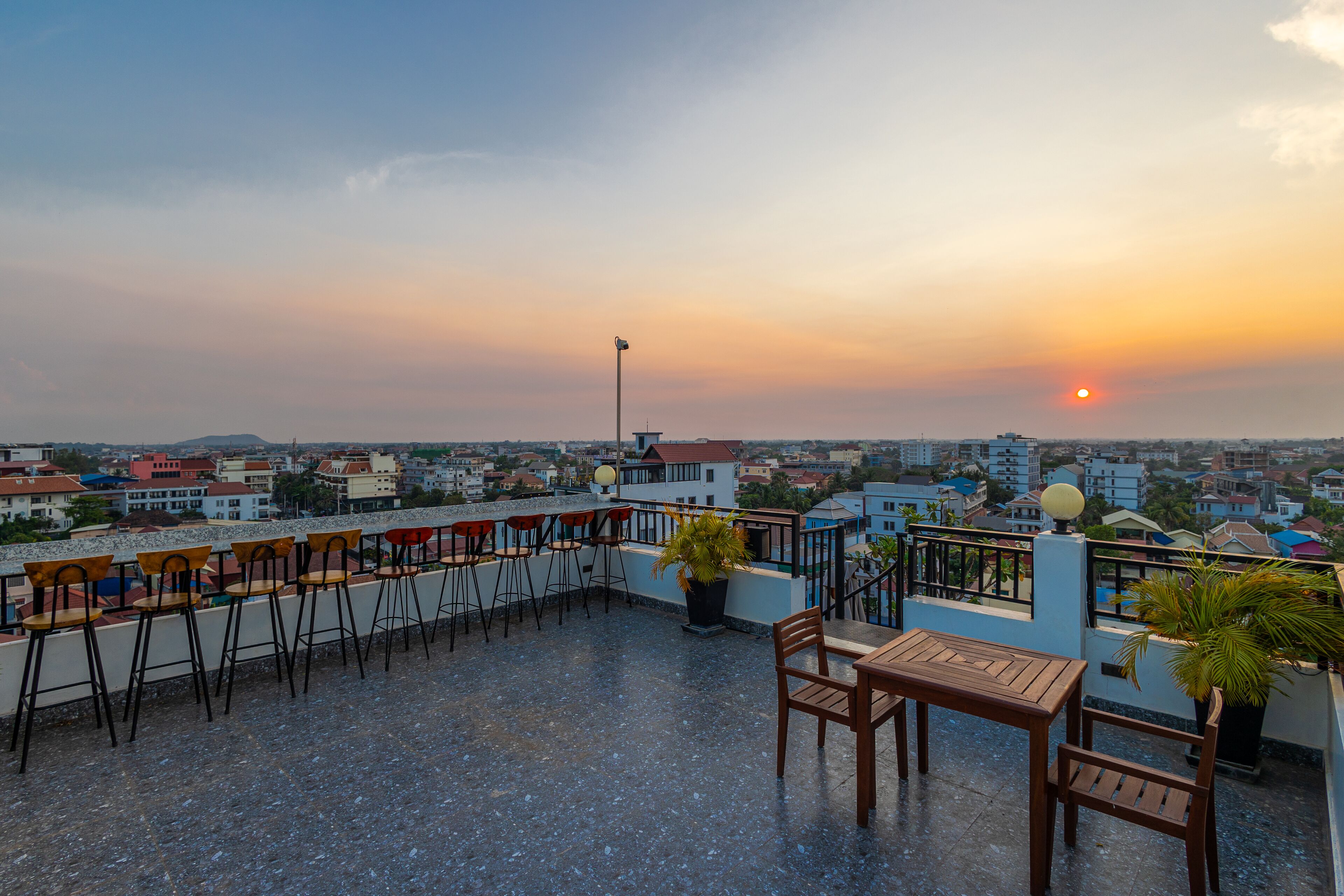 A rooftop terrace with outdoor seating, a view of the cityscape, and a sunset.