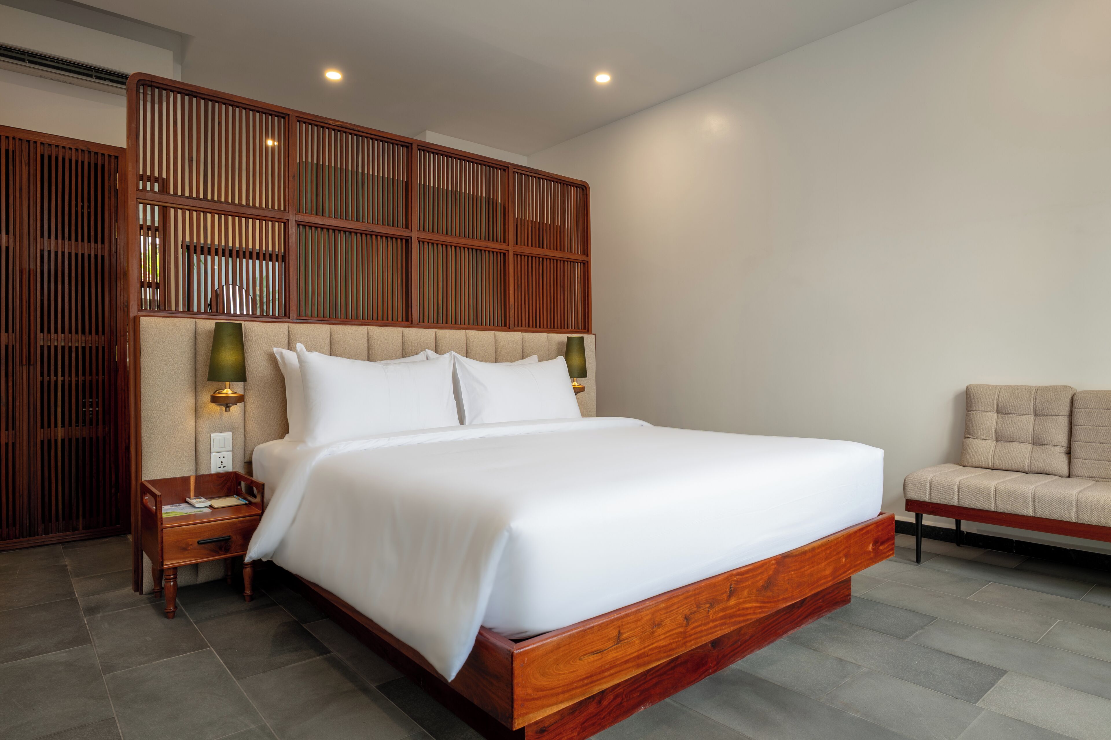 A modern hotel room with a large bed, wooden headboard, bedside tables, and a sofa.