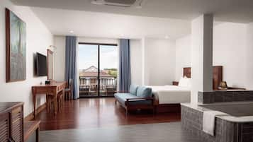 Una habitación de hotel moderna con una cama grande, un área de estar con un sofá y sillones, una mesa de comedor, un televisor y vistas al exterior.