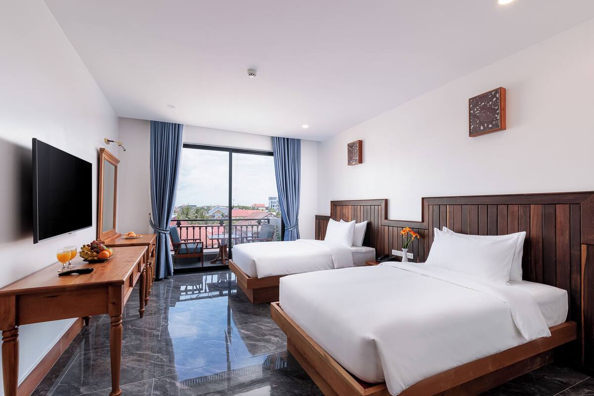 Une chambre d’hôtel avec deux lits, une télévision, un bureau avec un panier de fruits et un balcon avec vue.