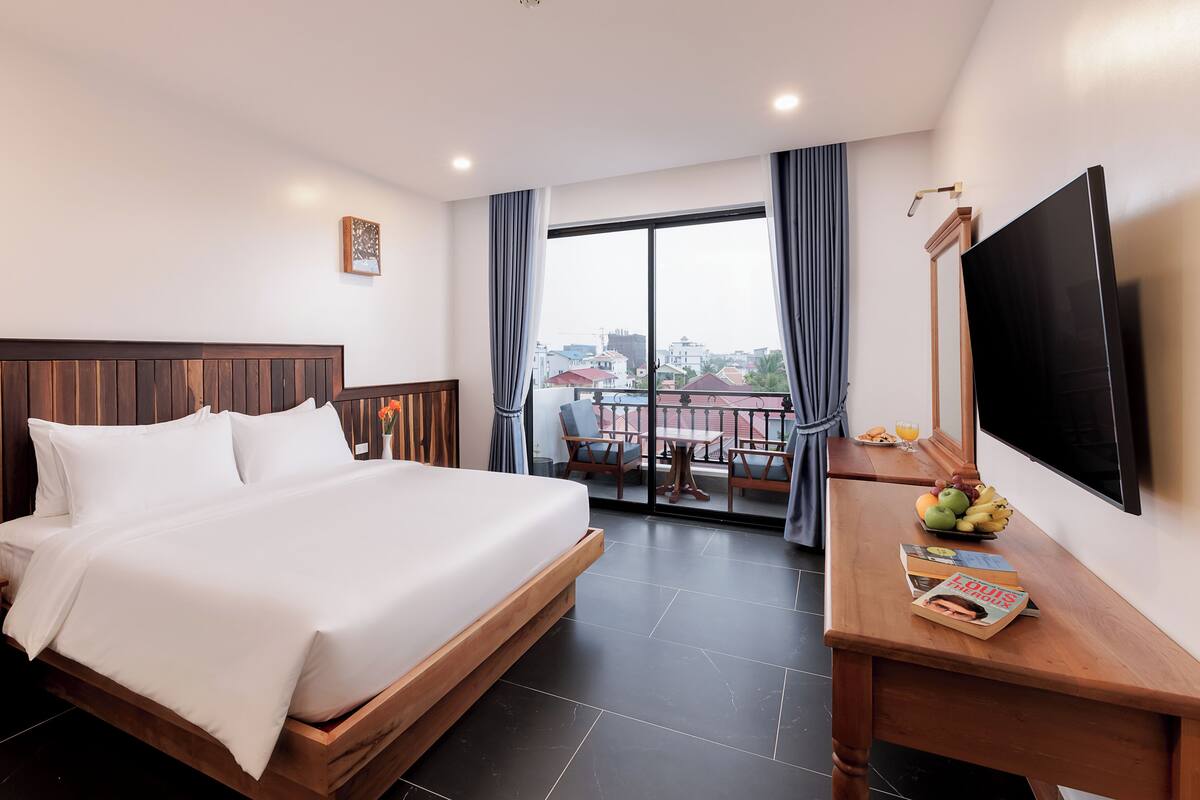 Une chambre d’hôtel comprenant un lit, un bureau avec un téléviseur à écran plat, une table à manger avec des chaises et un balcon offrant une vue sur la ville.