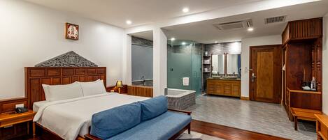 Een moderne hotelkamer met een houten bed, een blauwe bank, een badkamer met bad en een houten kledingkast.