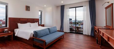 A hotel room with a large bed, a sofa, a desk, and a balcony with a view.