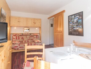 A cozy room with a wooden sofa, a dining table set for two, and a framed picture on the wall.