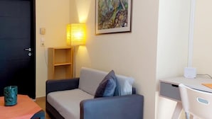 Una habitación pequeña y ordenada con un sofá, una lámpara, un cuadro y un escritorio con una silla.