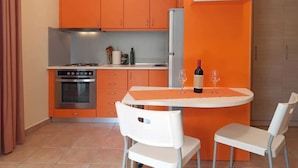 Una cocina compacta con armarios color naranja, un horno de acero inoxidable y una mesa de comedor blanca con dos sillas.