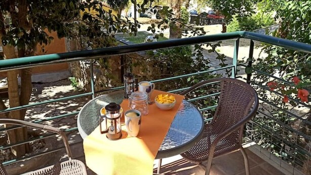 Una mesa redonda con mantel amarillo, una silla de metal y una barandilla metálica al fondo.