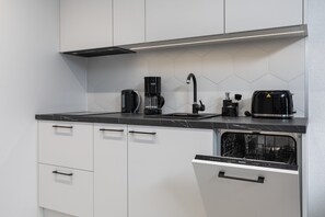 A modern kitchen with white cabinets, a black countertop, a coffee maker, a toaster, and a dishwasher.
