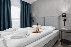 A hotel room with a bed, a bedside table, a lamp, and a window with curtains.