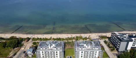 A coastal hotel with two main buildings, a beach in the background, and a clear view of the sea.