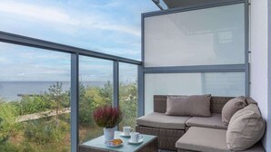 A balcony with a wicker sofa and a table with a plant and cups. - Modern Studio in Mielno | View of the Sea and Parking Lot (Mielno)