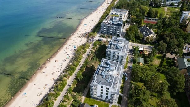 An aerial view of a coastal area with a beach, buildings, and greenery. - Modern Studio in Mielno | View of the Sea and Parking Lot (Mielno)