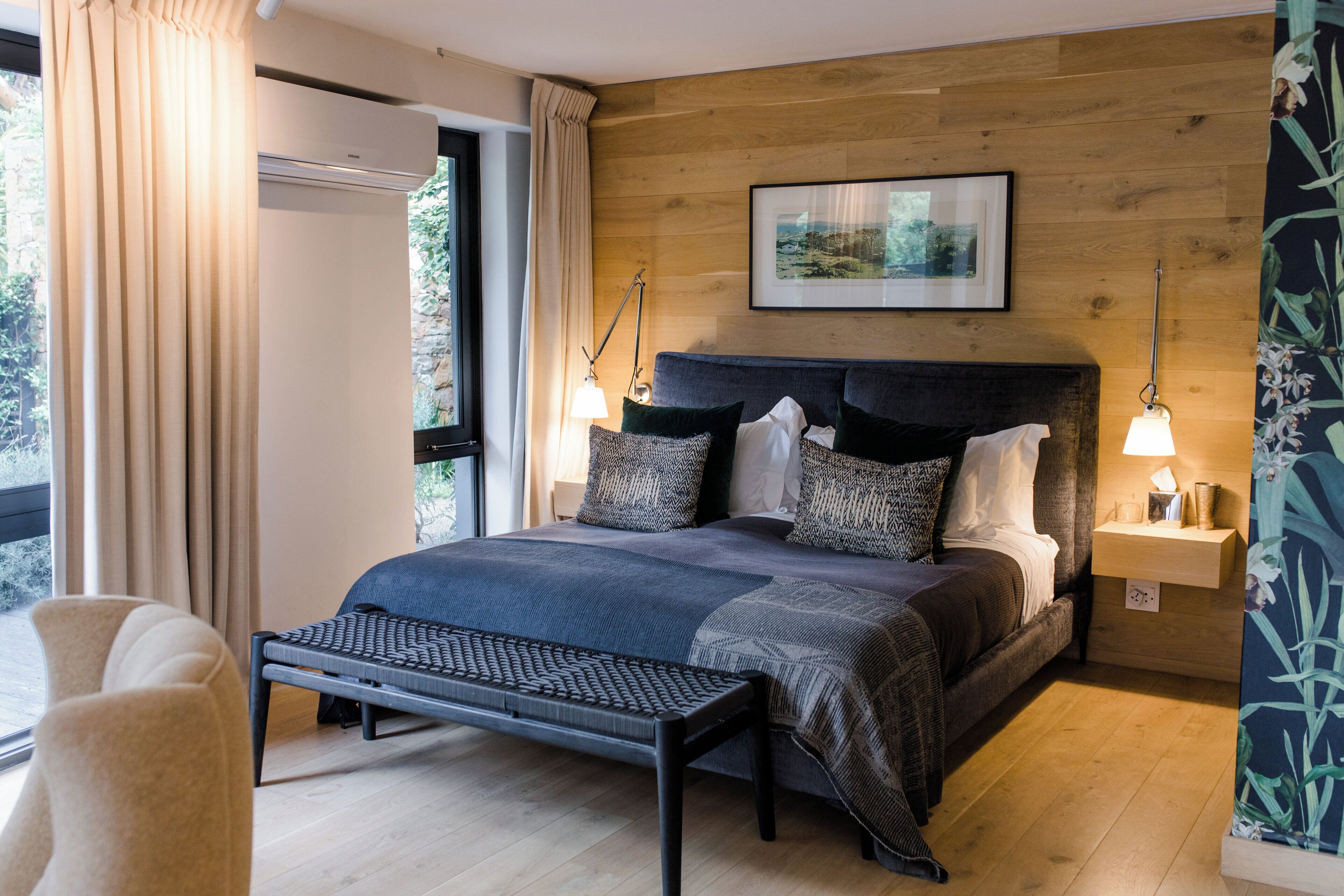Quarto moderno com uma cama grande, luminárias de cabeceira, um banquinho e vista pela janela.