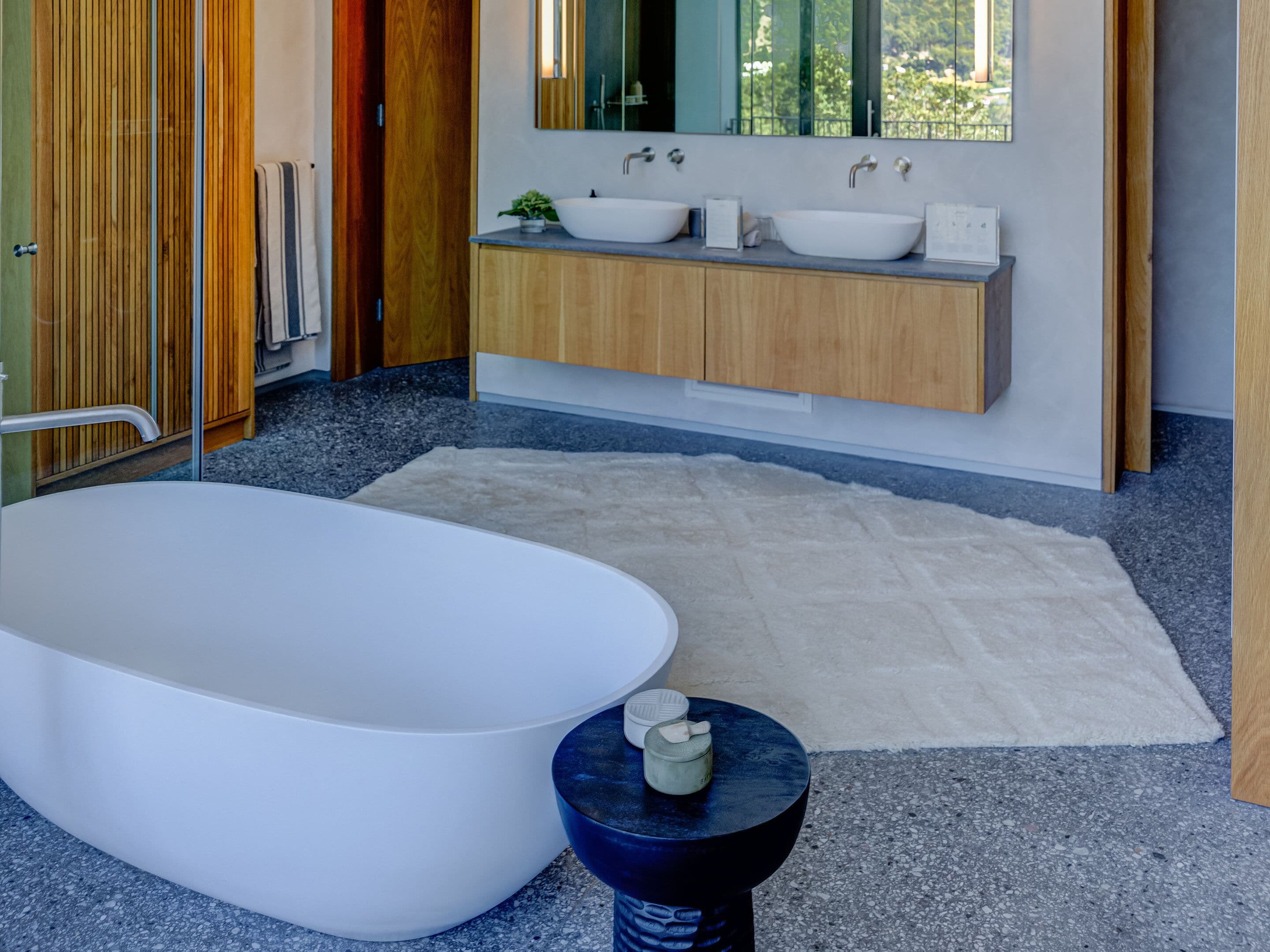 A modern bathroom with a freestanding bathtub, two sinks, and a wooden vanity.