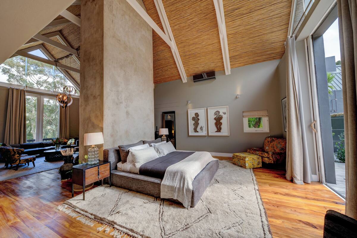 Un'ampia camera da letto con un letto grande, pavimento in legno e soffitto alto con travi a vista.