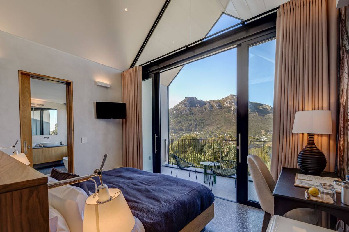 Camera d'albergo moderna con un ampio letto, una scrivania, una sedia, una televisione e un balcone con vista sulle montagne.