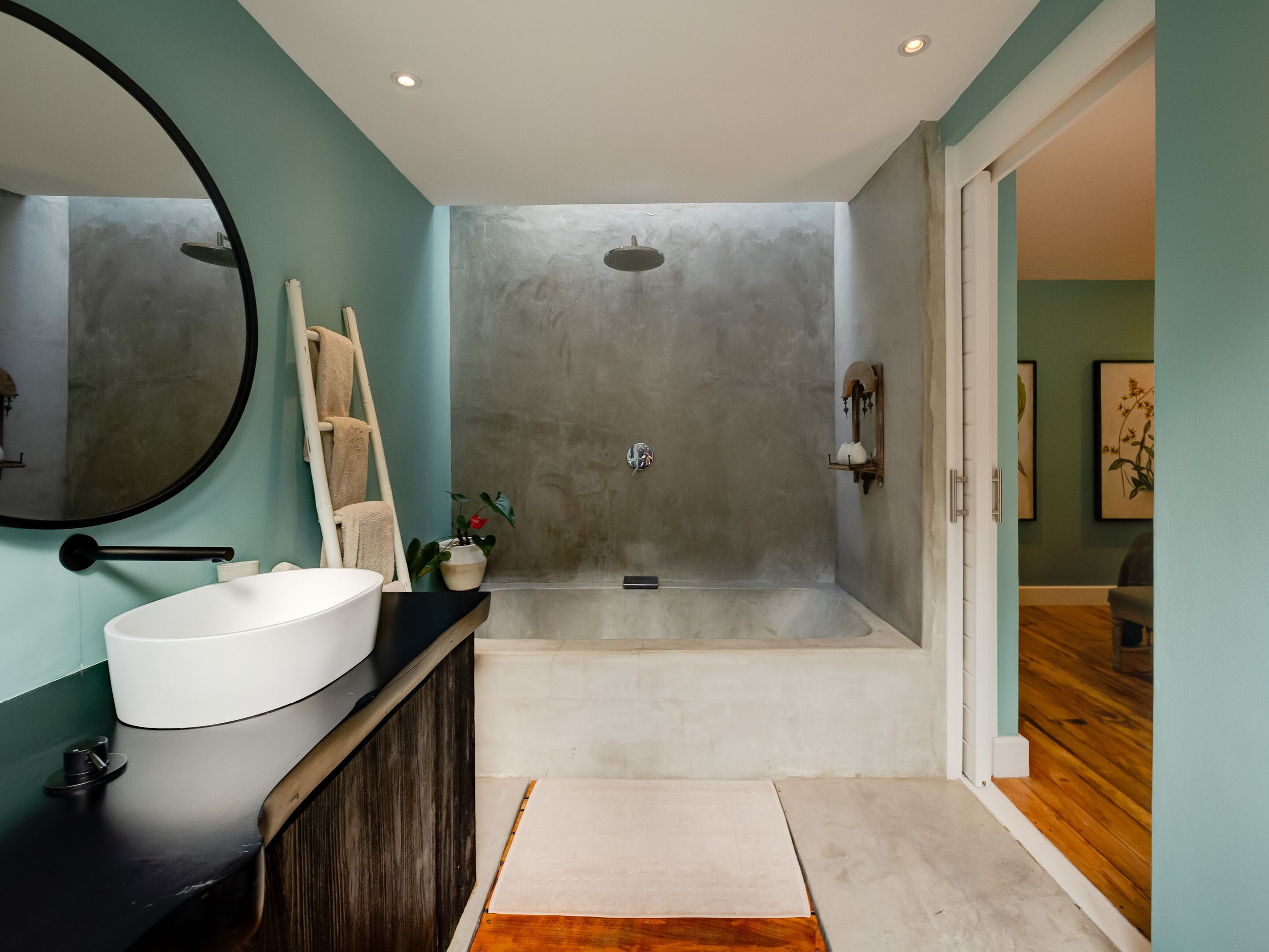 A modern bathroom with a large bathtub, a round mirror, and a wooden vanity.