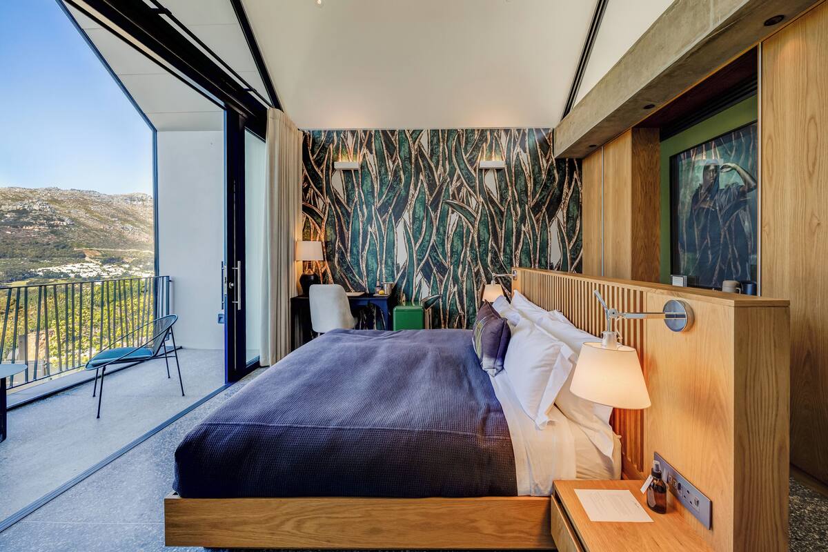 Una camera d'albergo moderna con un letto grande, una scrivania, una sedia e un balcone vista campagna.