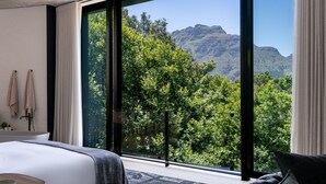 Un dormitorio moderno con una ventana grande, una cama, una mesita de noche y vistas a un paisaje montañoso.