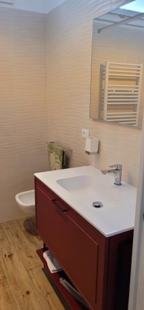 A modern bathroom with a white sink, red cabinet, and a white toilet.