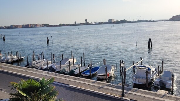 A marina with boats docked along a paved waterfront, a clear sky, and buildings in the background. - Appartamento Nuovo A Chioggia Vista Laguna (Chioggia)