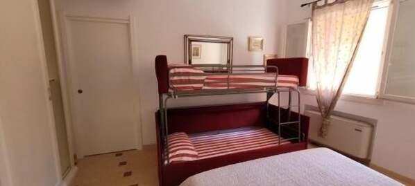 A bunk bed room with a white door, a radiator, and a window with curtains.
