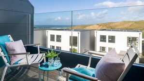 Een balkon met twee witte stoelen, een tafeltje met glazen en een plant, en uitzicht op zee en gebouwen.