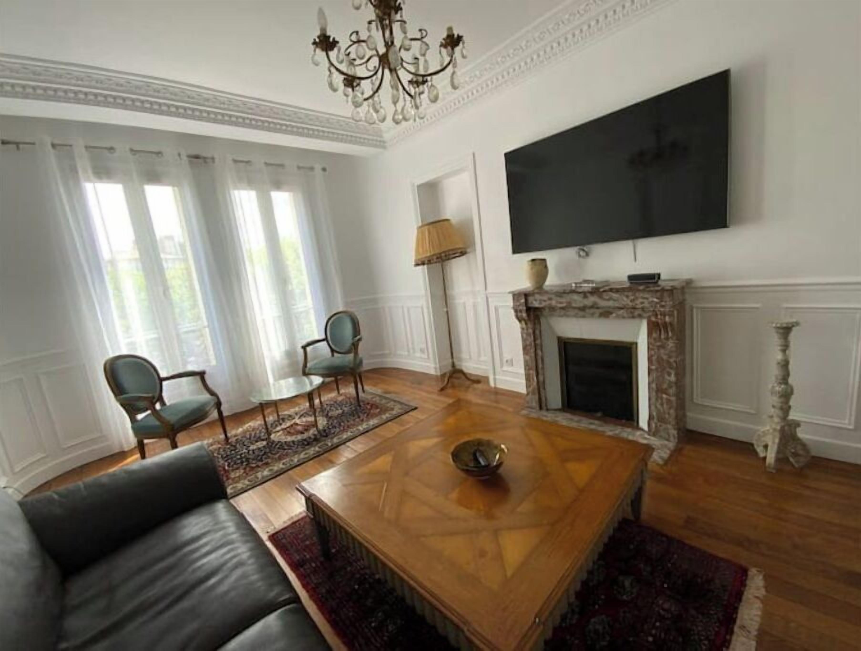 A living room with a fireplace, a television, and a chandelier.